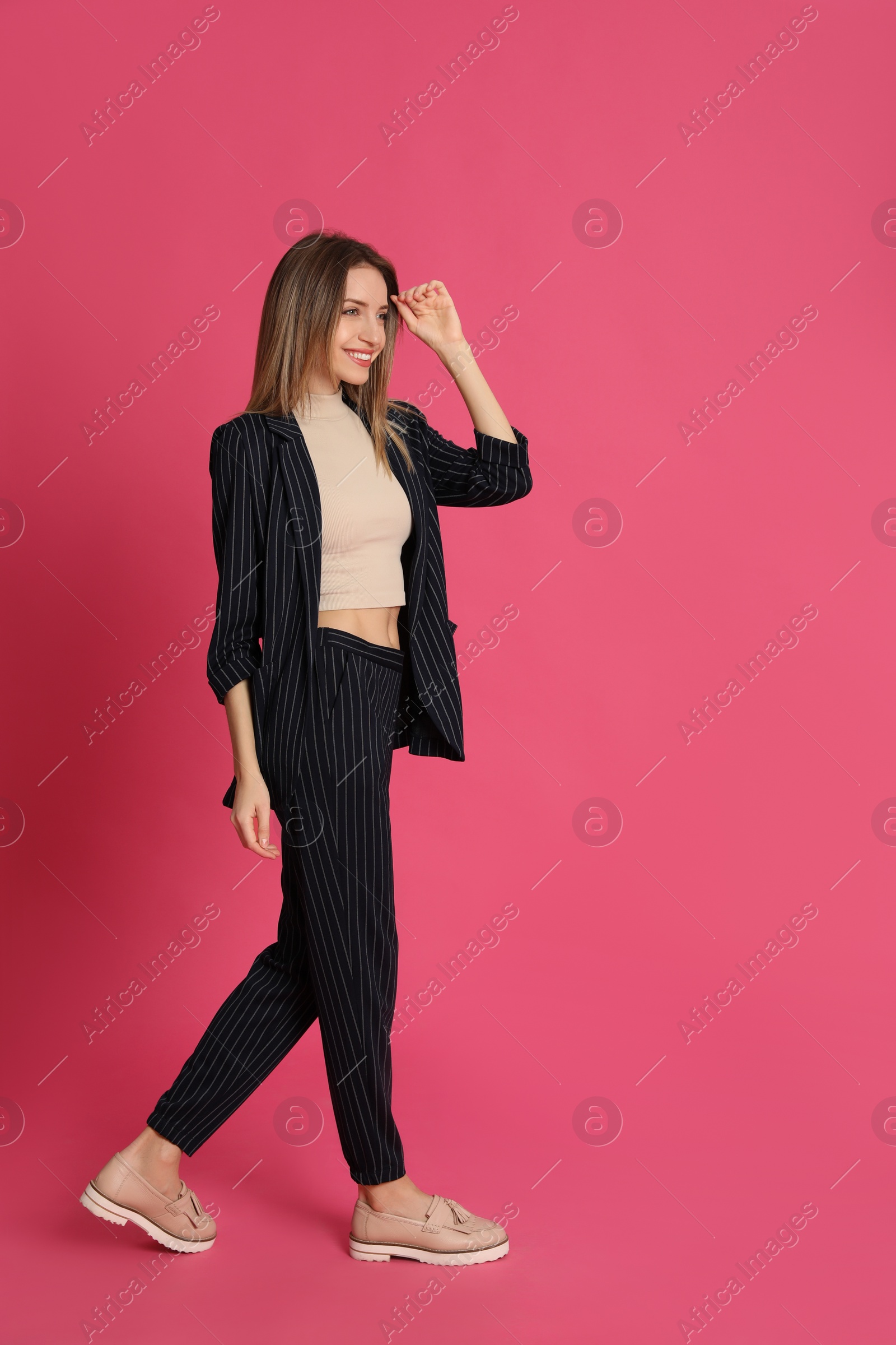 Photo of Full length portrait of beautiful young woman in fashionable suit on pink background. Business attire