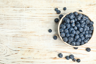 Tasty ripe blueberries in bowl on white wooden table, flat lay. Space for text