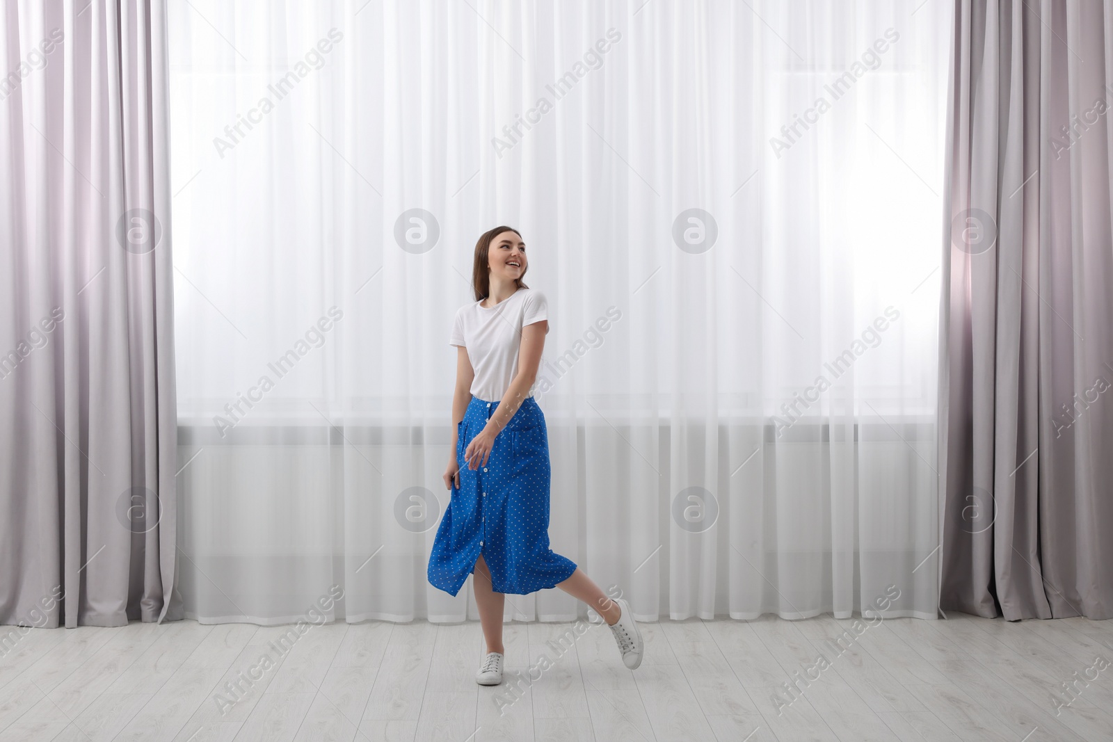 Photo of Woman standing near window with stylish curtains at home