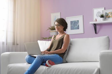 Photo of Young woman with modern laptop sitting on sofa at home