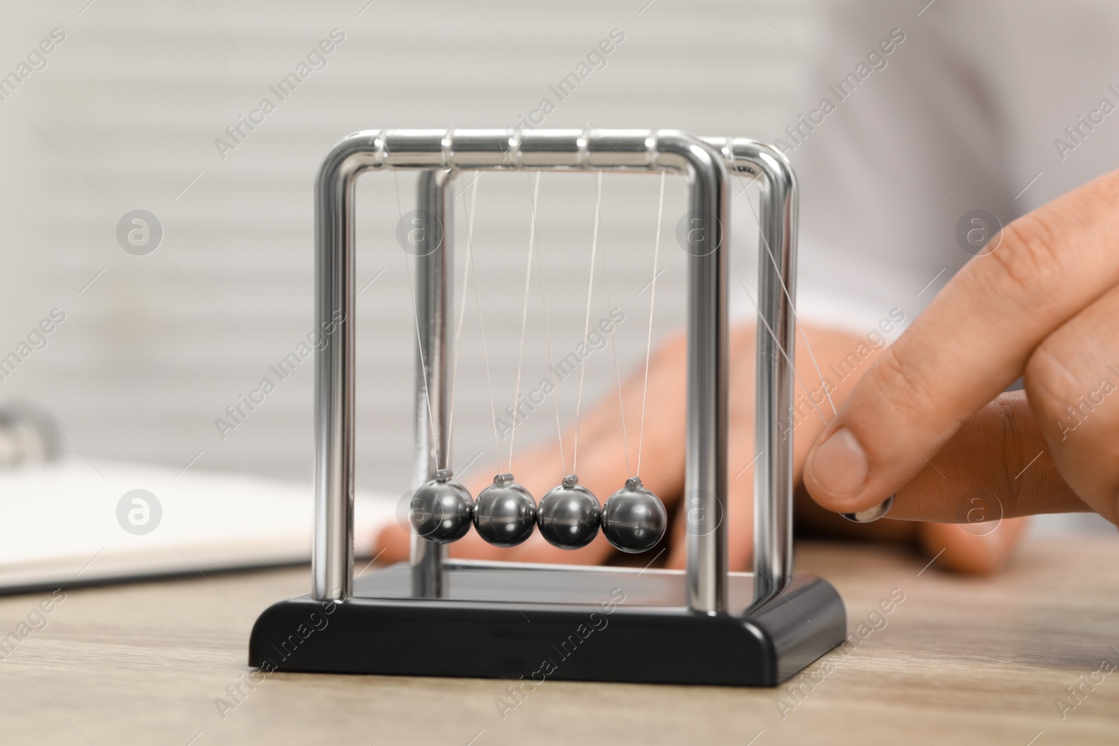 Photo of Man playing with Newton's cradle at wooden table, closeup. Physics law of energy conservation