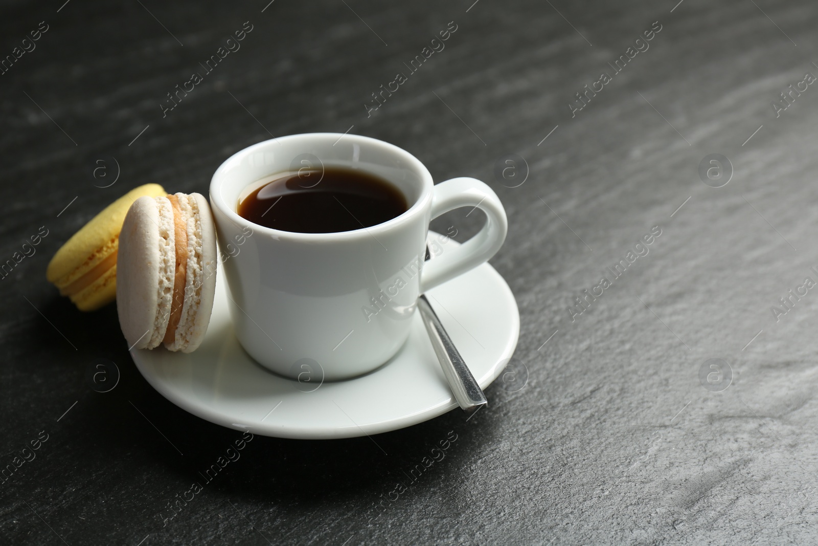 Photo of Hot coffee in cup, macarons and saucer on dark textured table, closeup. Space for text
