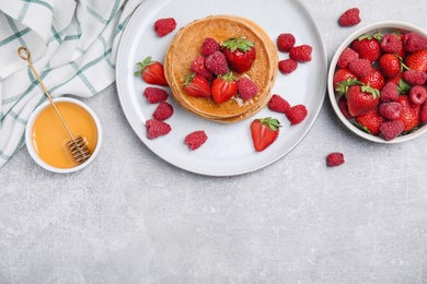 Tasty pancakes served with honey and berries on light grey table, flat lay. Space for text