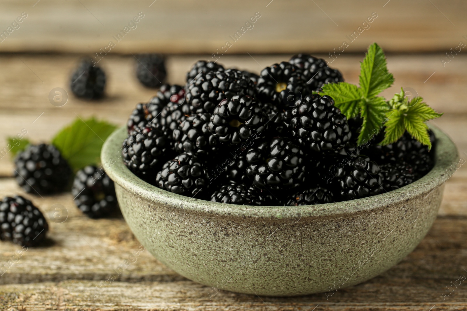 Photo of Bowl with fresh ripe blackberries on wooden table, closeup