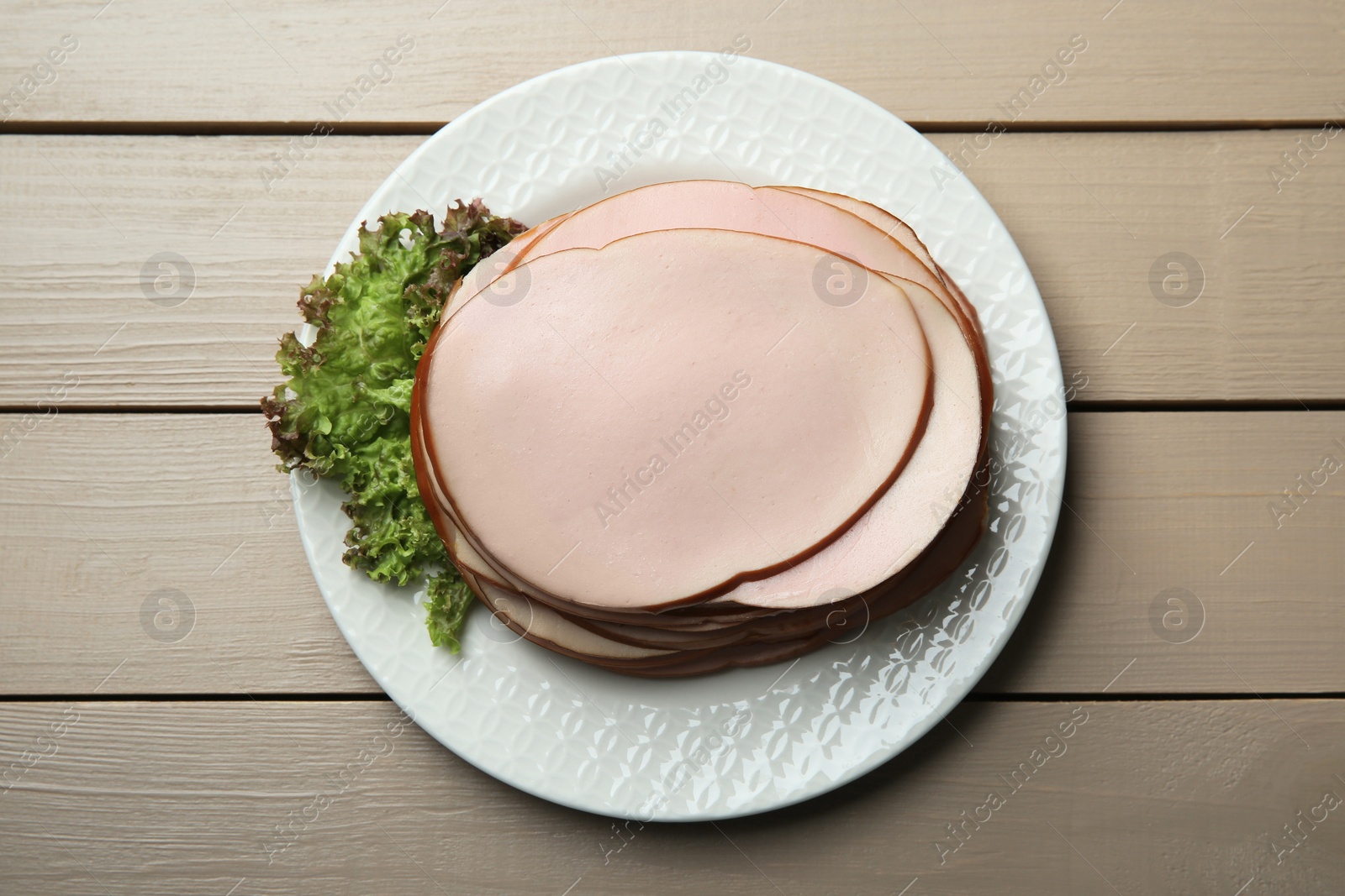 Photo of Slices of delicious boiled sausage with lettuce on beige wooden table, top view