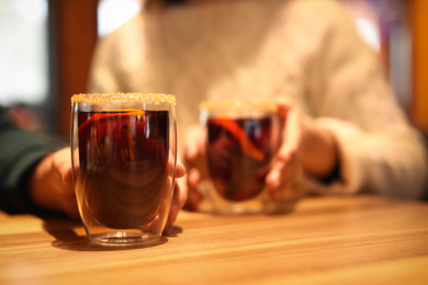 Photo of Lovely couple with tasty mulled wine at table in cafe, closeup