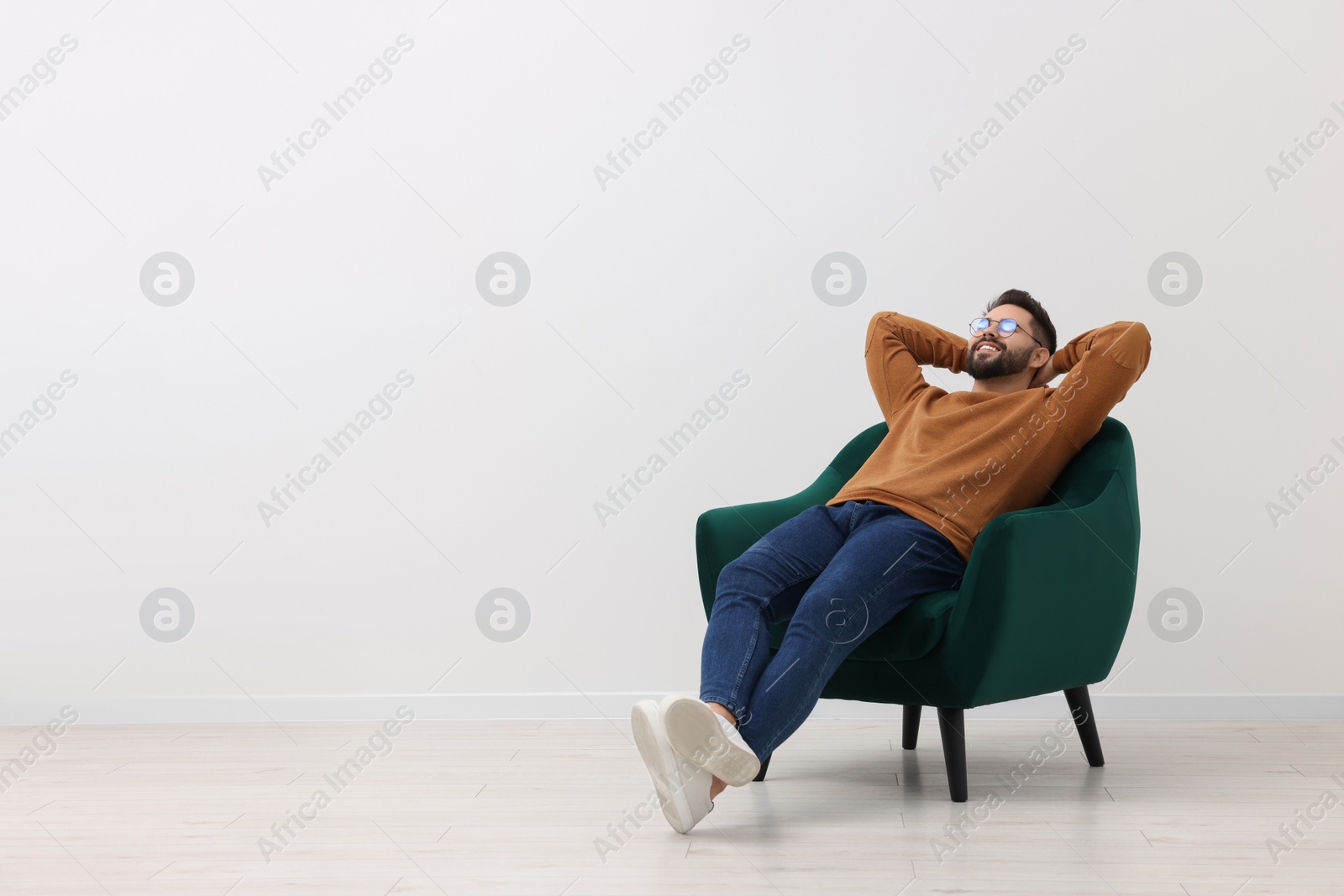 Photo of Handsome man relaxing in armchair near white wall indoors, space for text