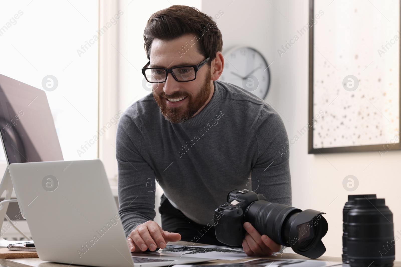 Photo of Professional photographer with digital camera using laptop in office