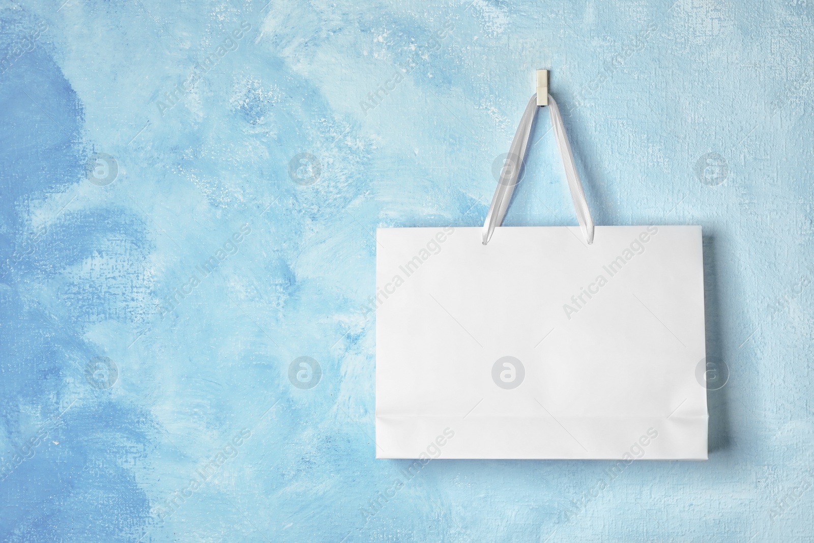 Photo of Paper shopping bag with handles hanging on color wall. Mock up for design