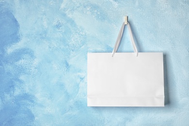 Paper shopping bag with handles hanging on color wall. Mock up for design