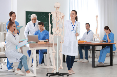 Medical students and professor studying human skeleton anatomy in classroom