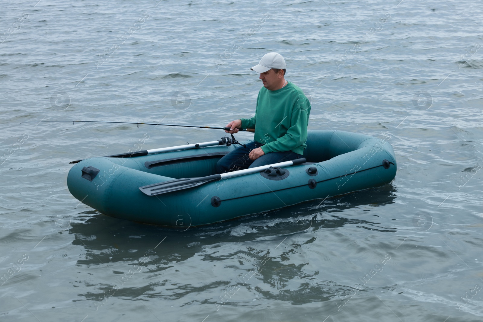 Photo of Man fishing with rod from inflatable rubber boat on river