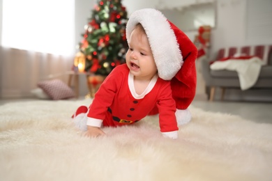 Photo of Cute little baby in Christmas costume crawling on fur rug at home