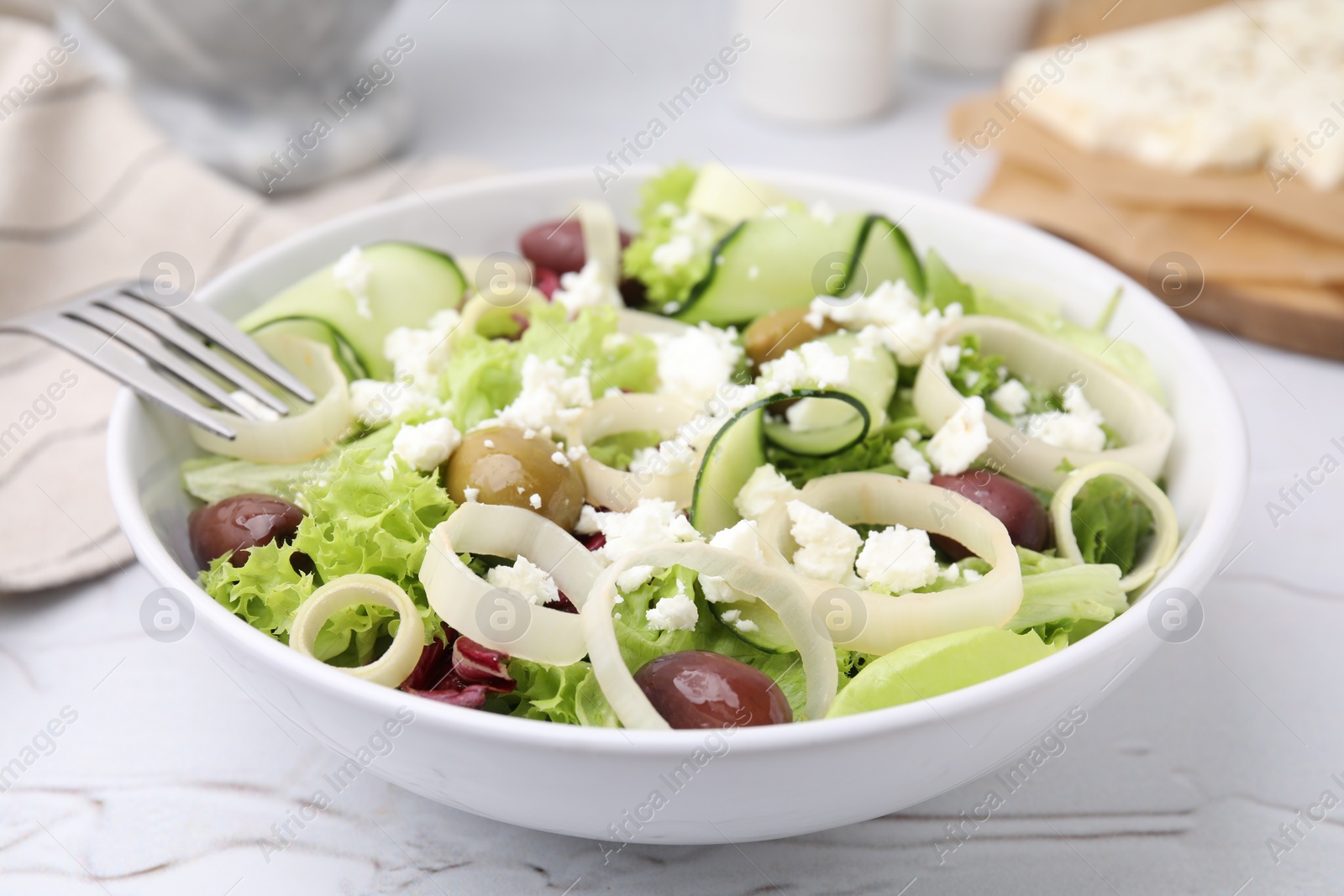 Photo of Bowl of tasty salad with leek, olives and cheese on white marble table, closeup