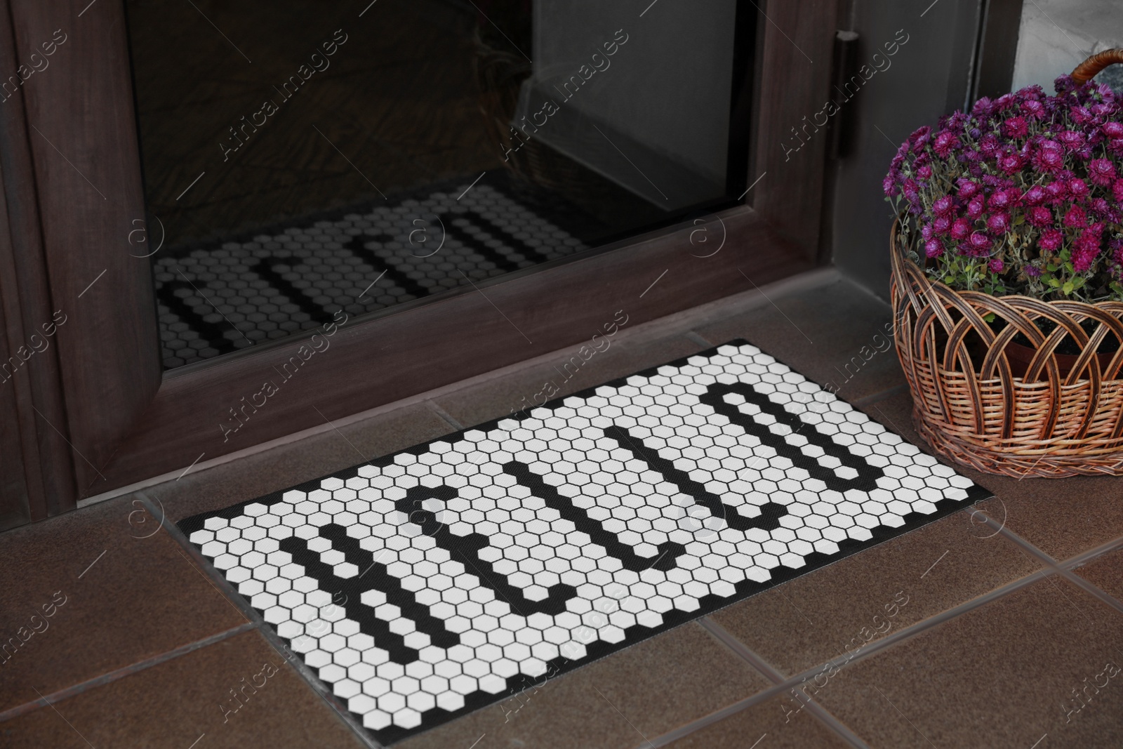 Photo of Stylish door mat with word HELLO and beautiful flowers near entrance