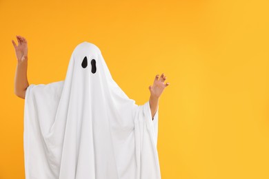 Photo of Woman in white ghost costume on yellow background, space for text. Halloween celebration