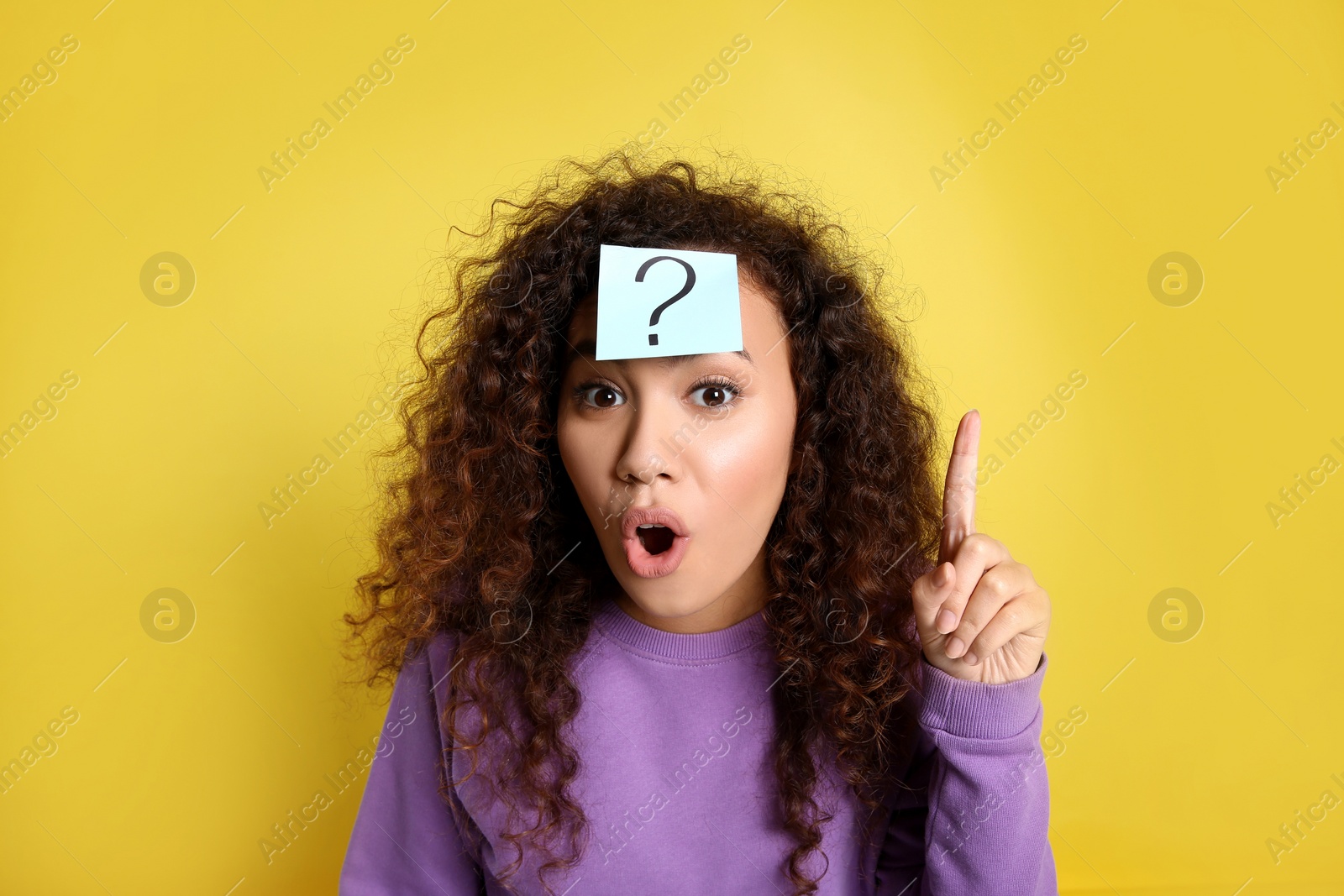 Photo of Emotional African-American woman with question mark sticker on forehead against yellow background
