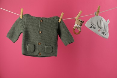 Baby clothes and accessories hanging on washing line against pink background