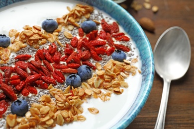 Photo of Smoothie bowl with goji berries and spoon on wooden table, closeup