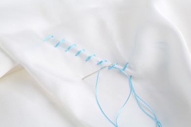 Photo of Sewing needle with thread and stitches on white cloth, closeup
