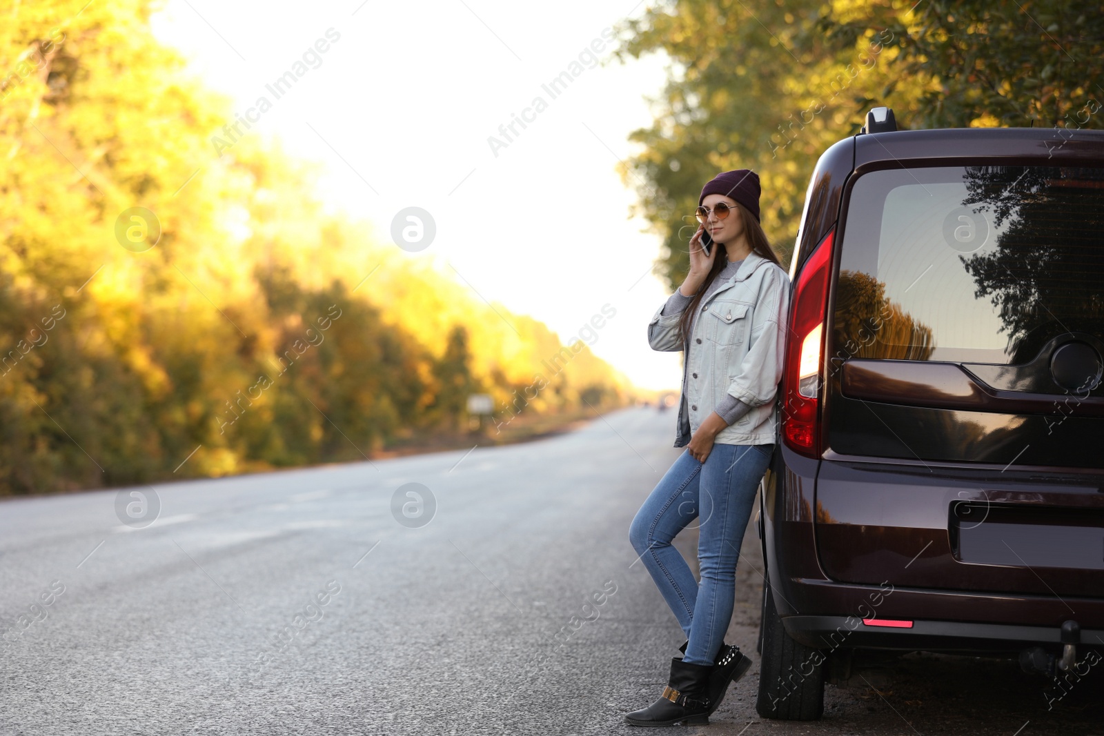 Photo of Young woman with mobile phone near car on country road. Space for text