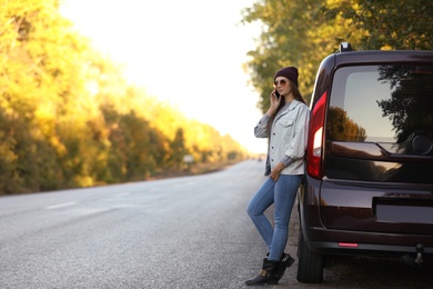 Young woman with mobile phone near car on country road. Space for text