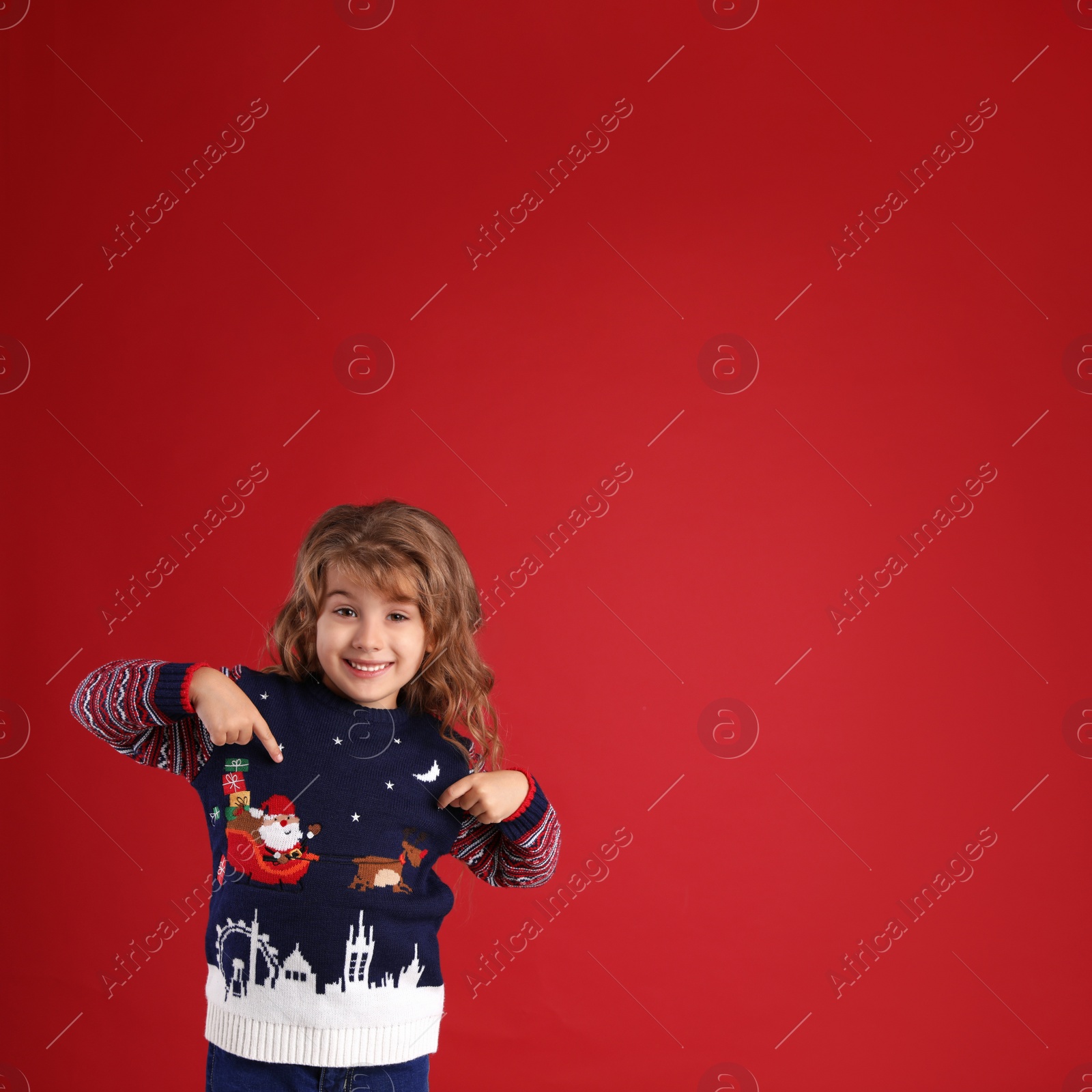 Photo of Cute little girl pointing at her Christmas sweater against red background. Space for text