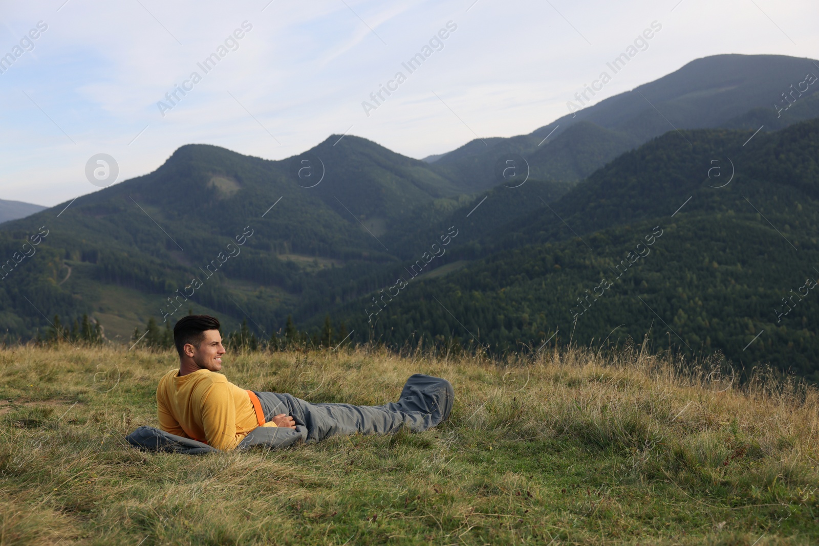 Photo of Man in sleeping bag enjoying mountain landscape, space for text