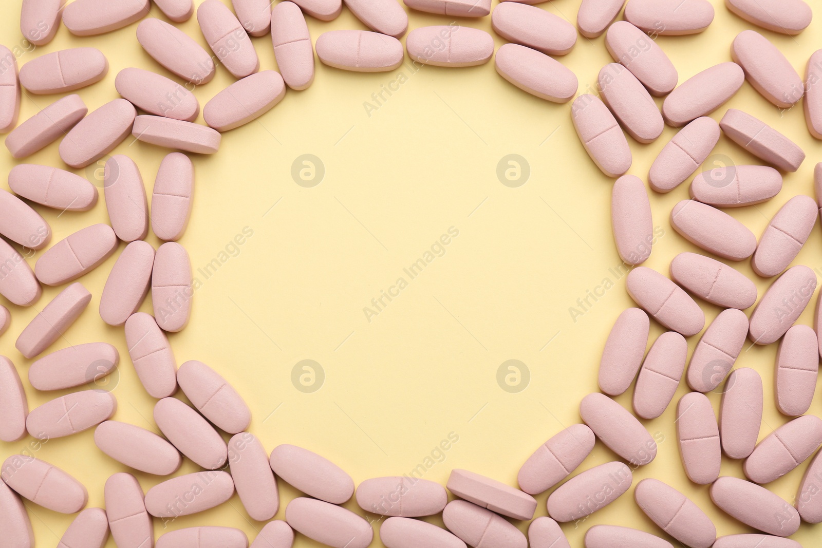 Photo of Frame made of vitamin pills on pale yellow background, top view. Space for text