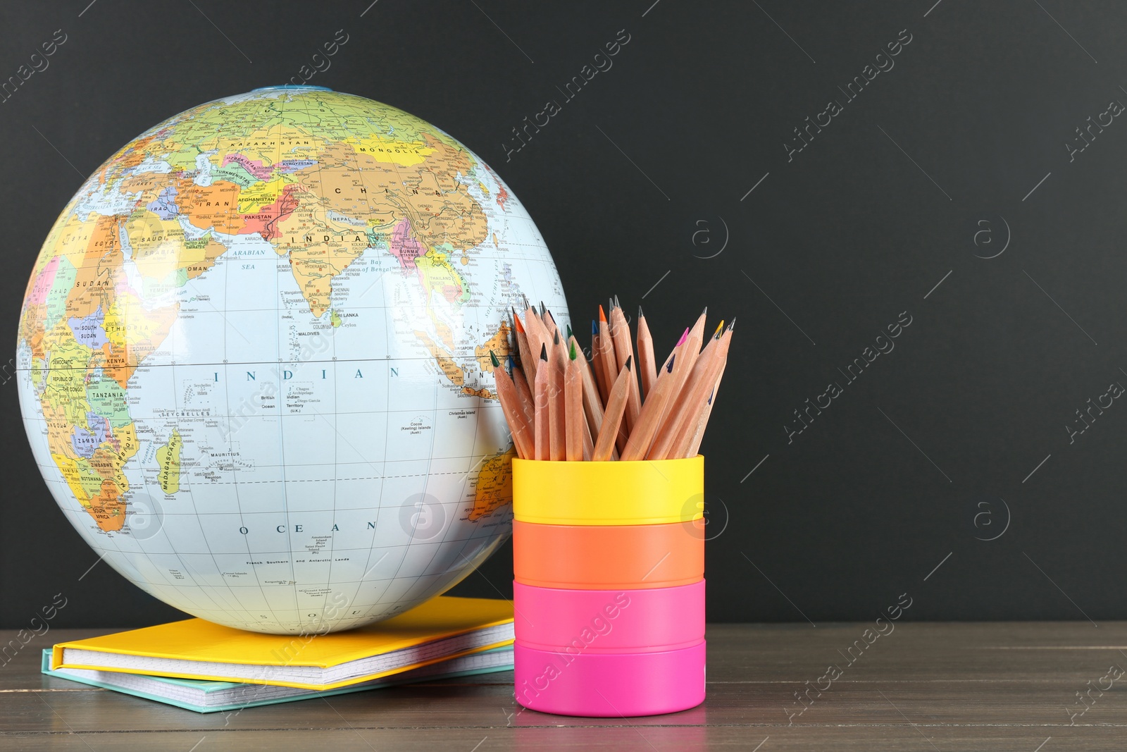 Photo of Globe, books and school supplies on wooden table near black chalkboard, space for text. Geography lesson