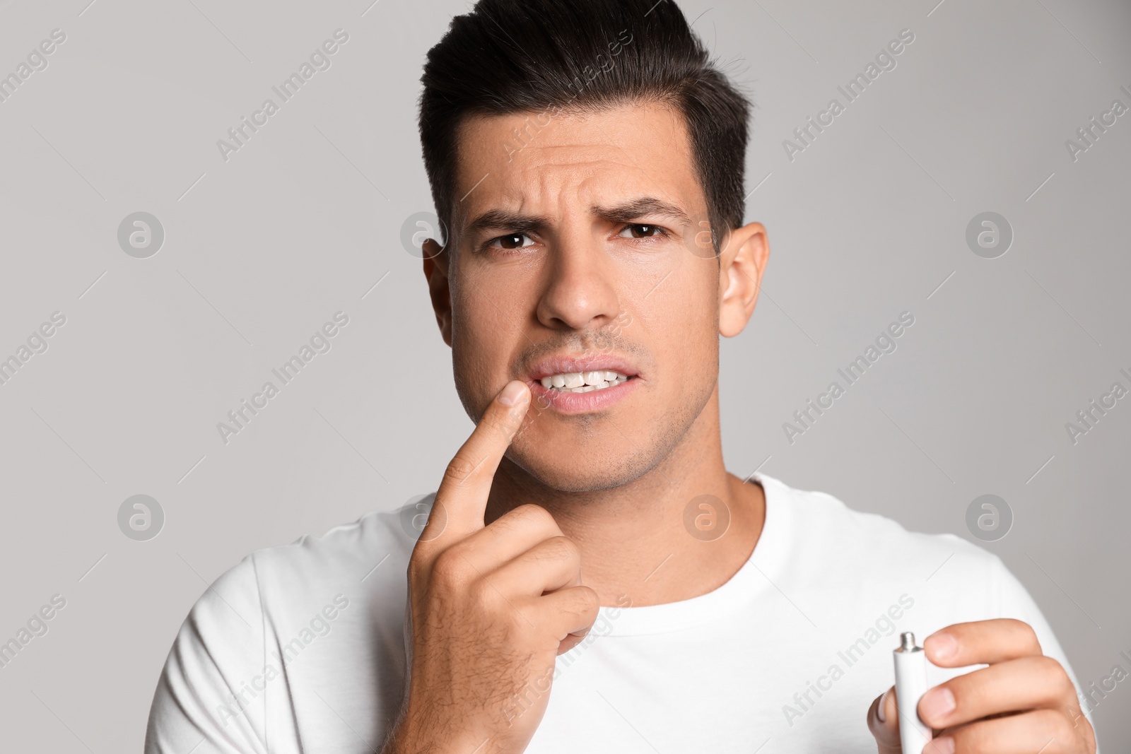 Photo of Emotional man with herpes applying cream on lips against light grey background