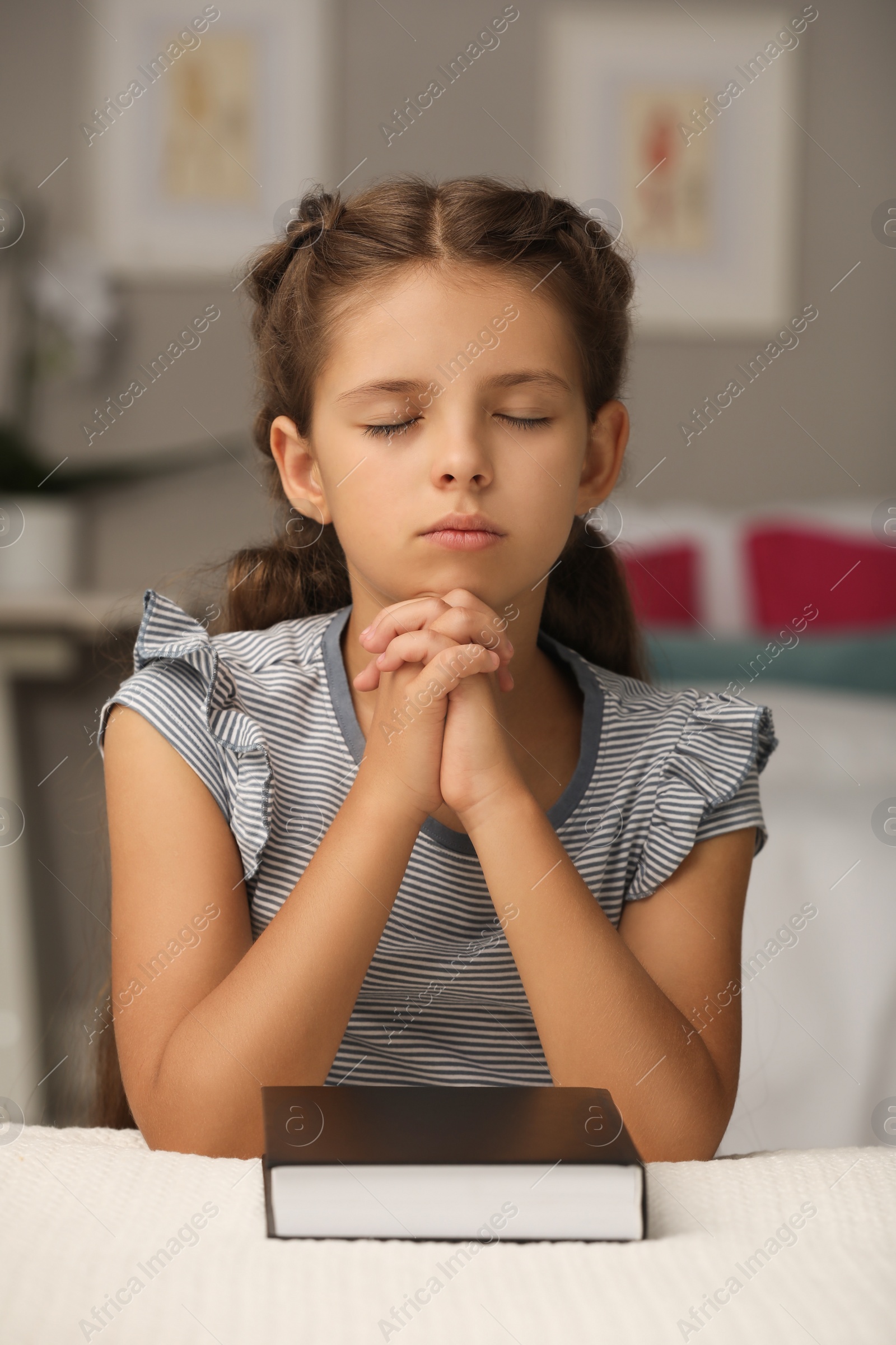 Photo of Cute little girl praying over Bible in bedroom