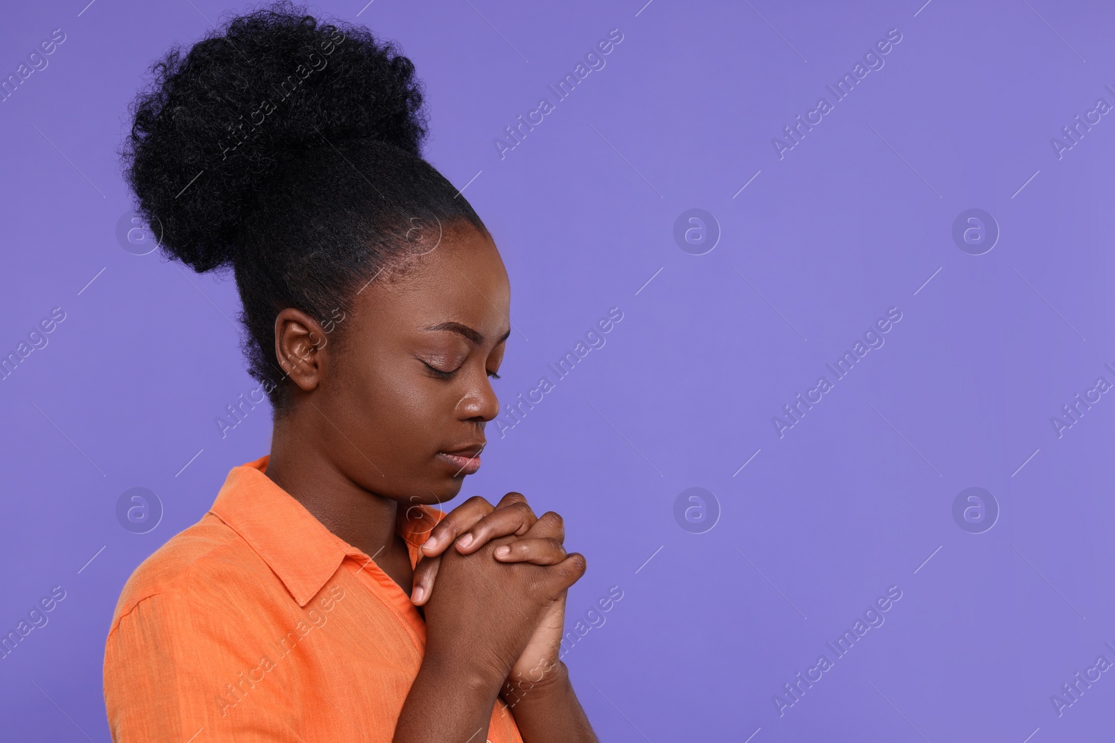 Photo of Woman with clasped hands praying to God on purple background. Space for text