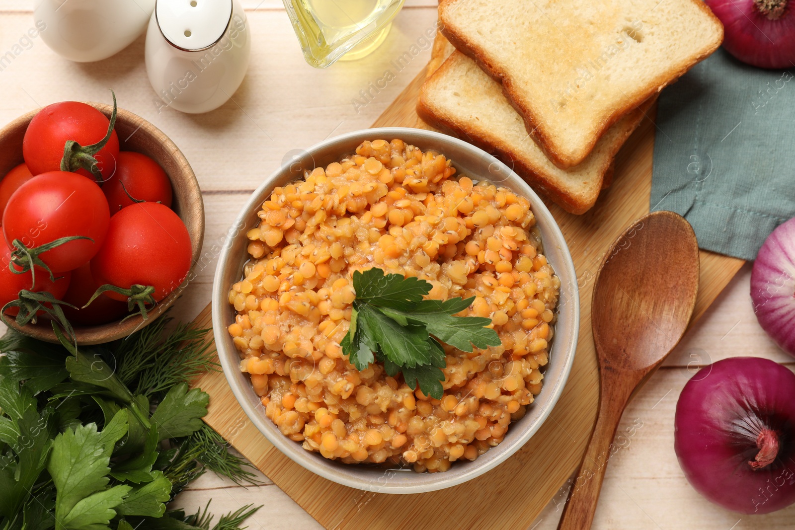 Photo of Delicious red lentils with parsley in bowl served on table, flat lay