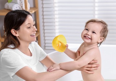 Mother bathing her cute little baby in tub at home