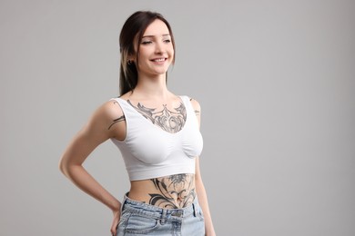 Portrait of smiling tattooed woman on grey background. Space for text