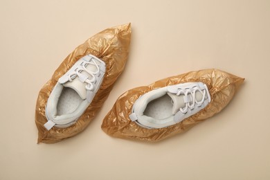 Photo of Sneakers in shoe covers on beige background, top view