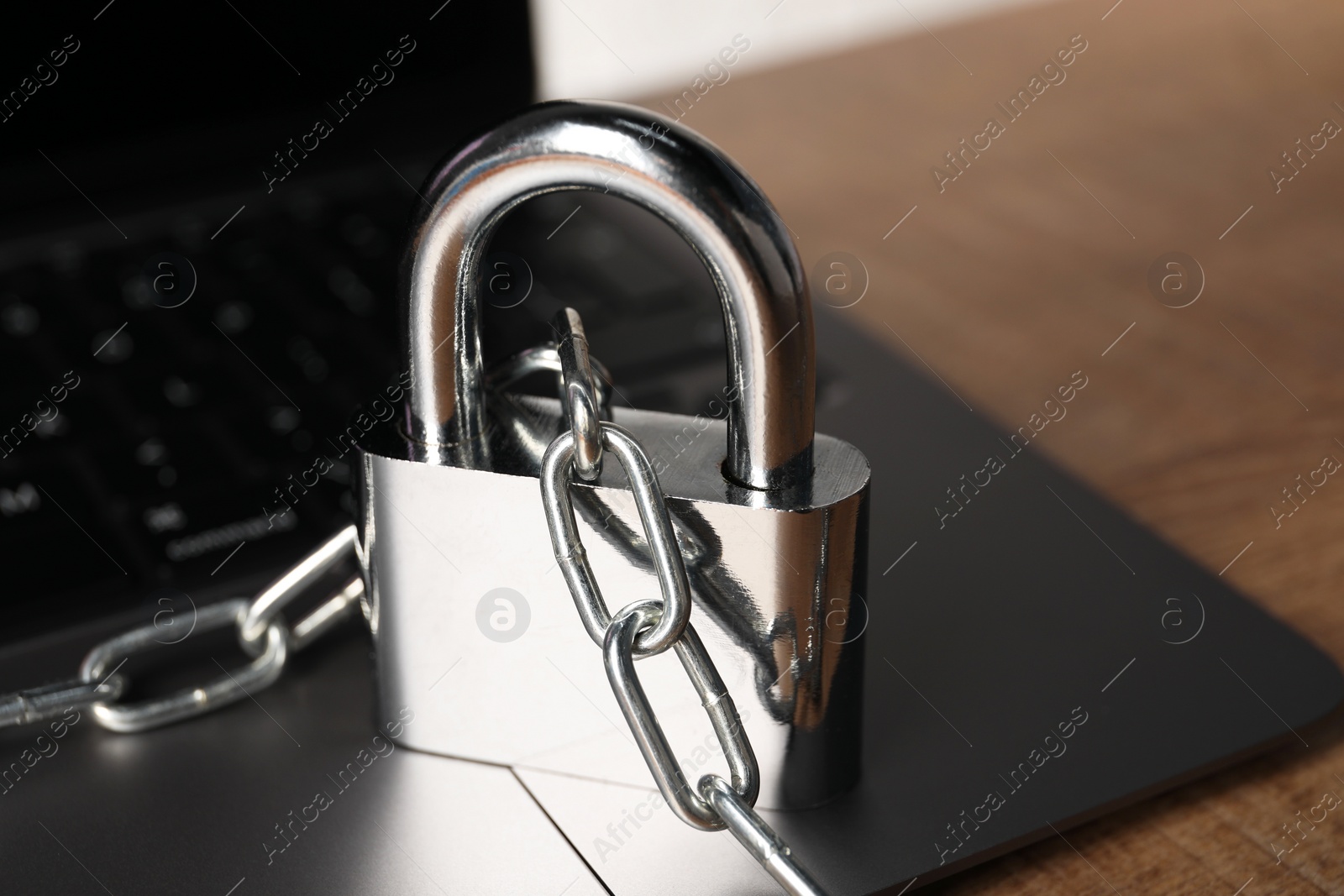 Photo of Cyber security. Laptop with padlock and chain on wooden table, closeup