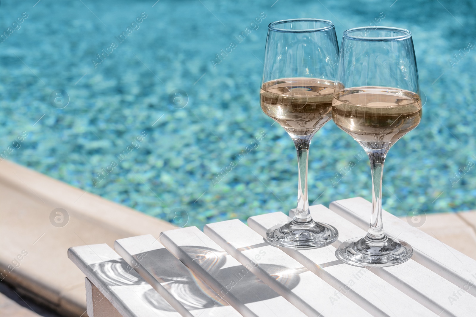 Photo of Glasses of tasty wine on wooden table near swimming pool, space for text