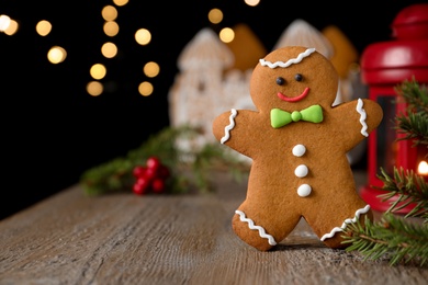 Photo of Gingerbread man on wooden table against blurred lights, closeup. Space for text