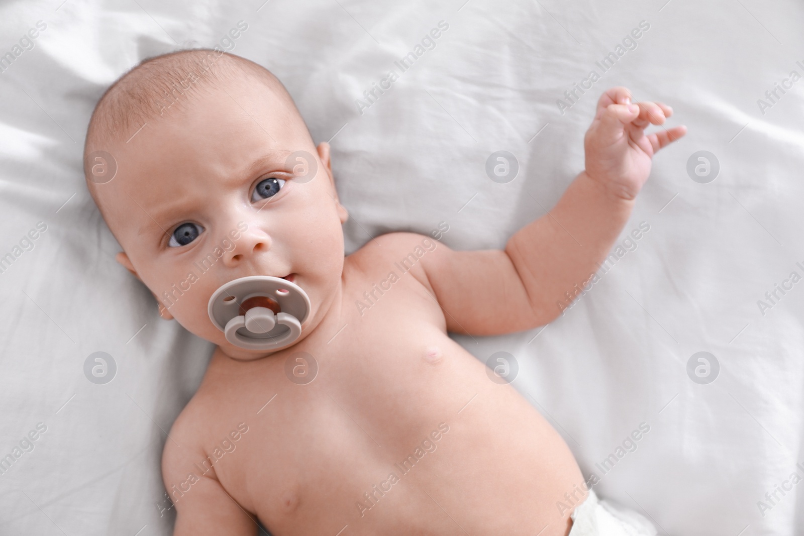 Photo of Cute little baby with pacifier lying on bed, top view