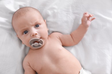 Cute little baby with pacifier lying on bed, top view