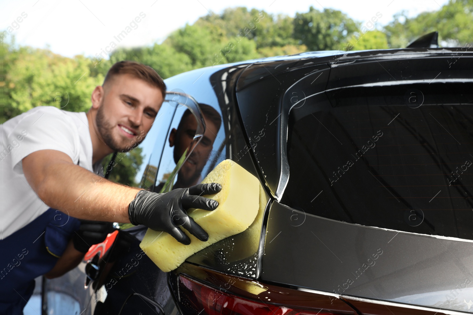 Photo of Young worker cleaning automobile with sponge at car wash