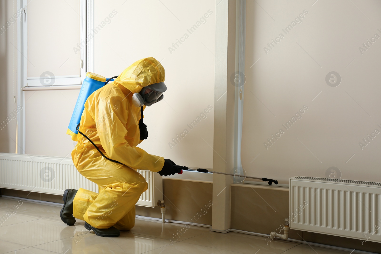 Photo of Pest control worker in protective suit spraying pesticide indoors. Space for text