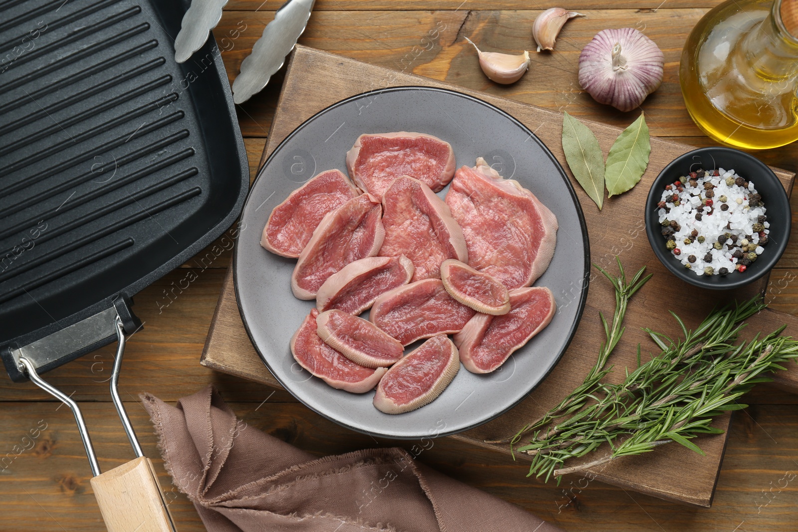 Photo of Raw beef tongue pieces, pan and spices on wooden table, flat lay