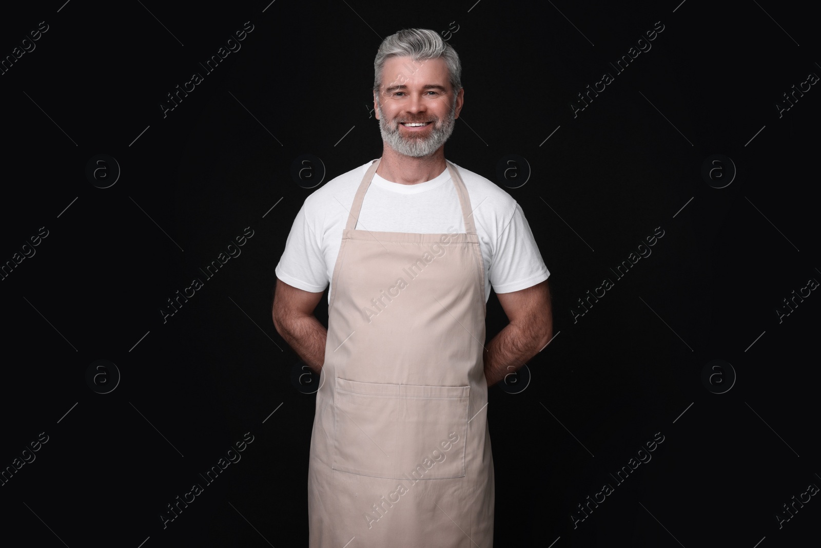 Photo of Happy man wearing kitchen apron on black background. Mockup for design