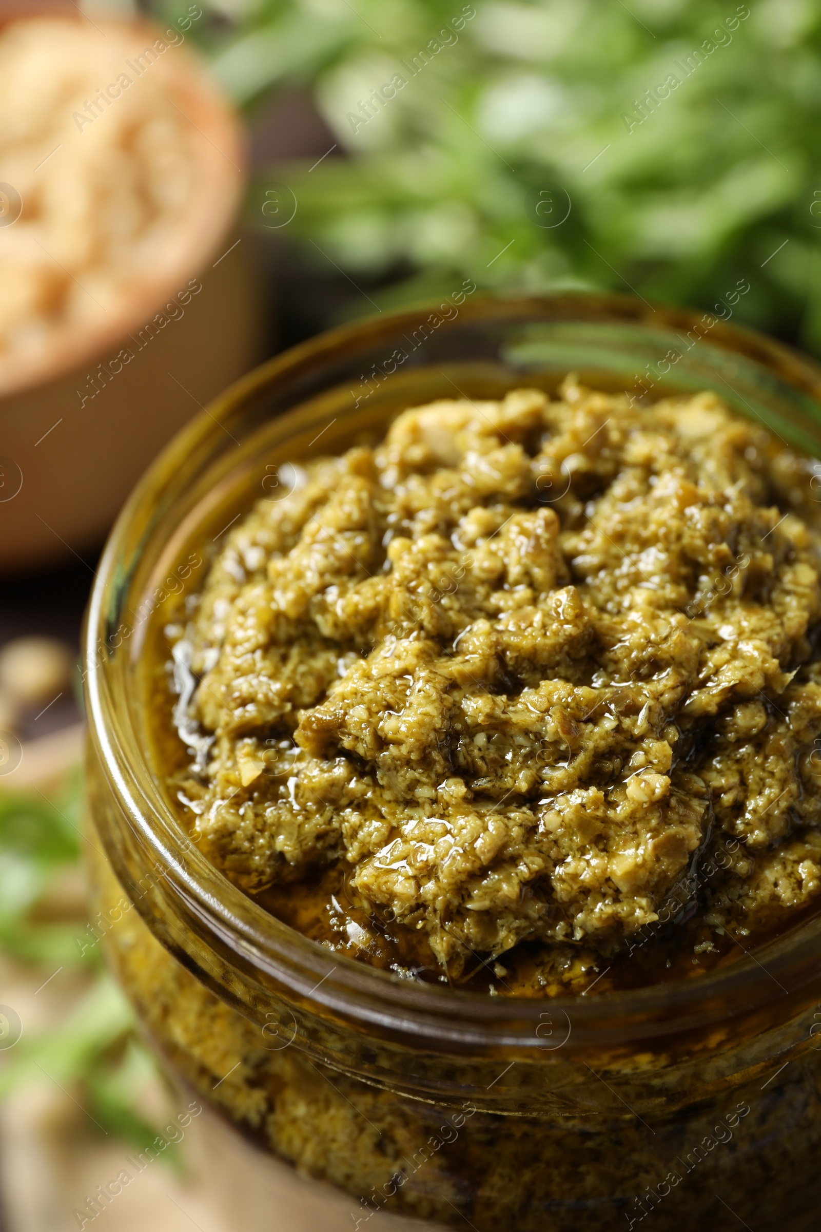 Photo of Jar of tasty arugula pesto on table, closeup