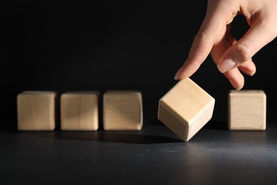 Photo of Woman choosing wooden cube among others at dark table, closeup