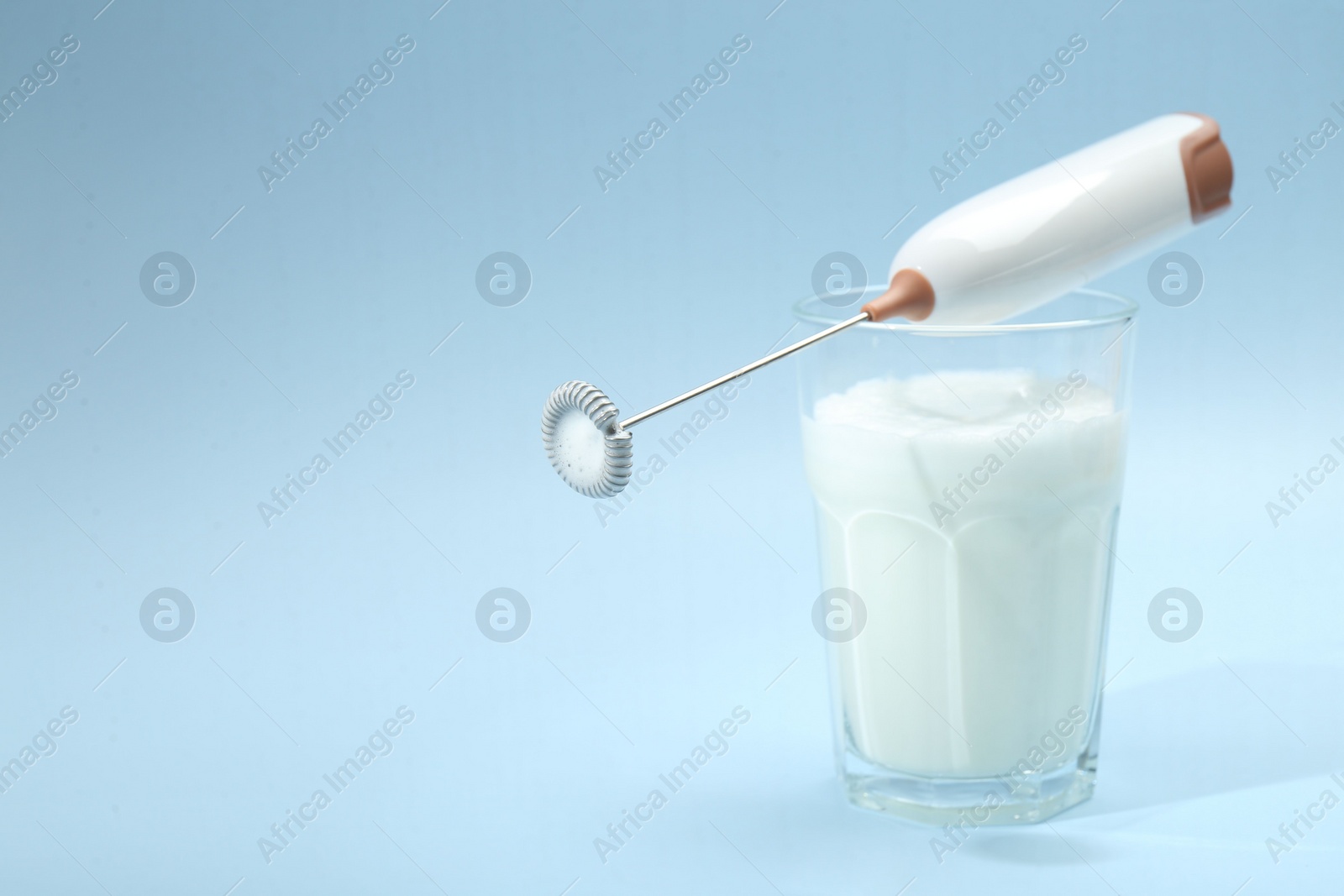 Photo of Mini mixer (milk frother) and whipped milk in glass on light blue background. Space for text