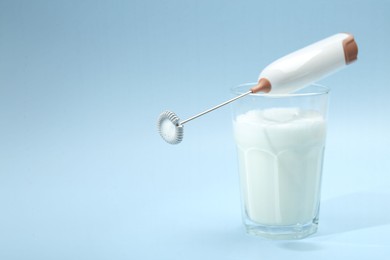 Mini mixer (milk frother) and whipped milk in glass on light blue background. Space for text